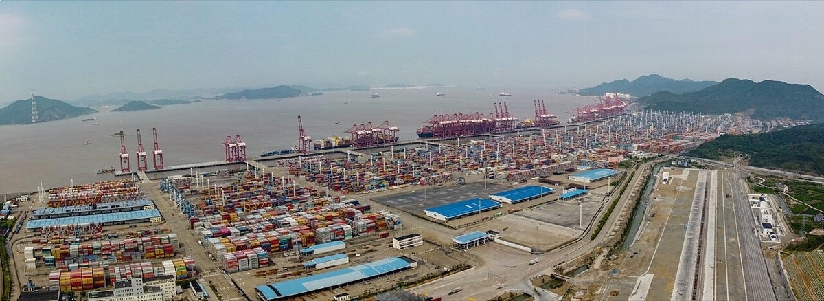 A wide shot of a Chinese export container terminal at night with gantry cranes working vessels, capturing the backlog moving through ports as GACC reports the December 2022 export contraction